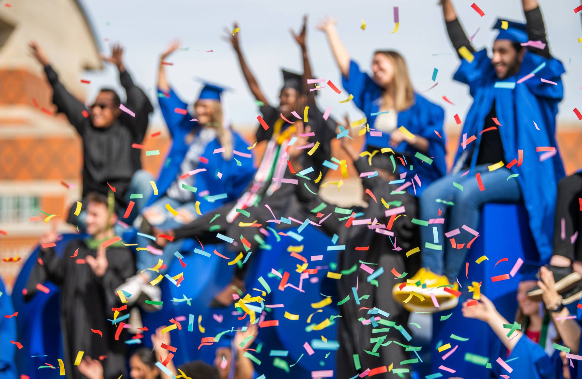 Students celebrating granduation in caps and gowns with confetti.